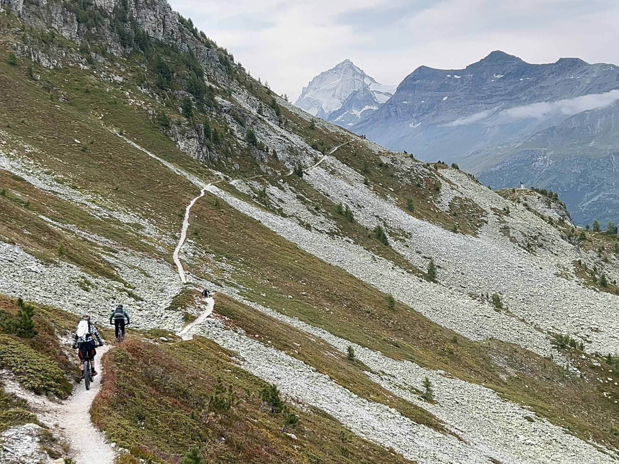 Two riders on a balcony singletrack facing the peaks of Valais, 2027 MTB season with Exoride