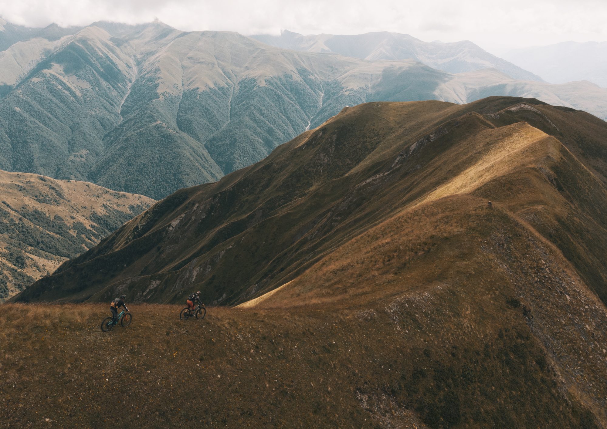 Two riders on a golden Caucasus ridge, facing the peaks, preparing for an MTB trip with Exoride